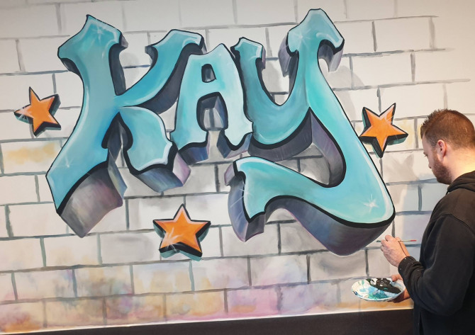 Kay in grafitti-letters in speelruimte